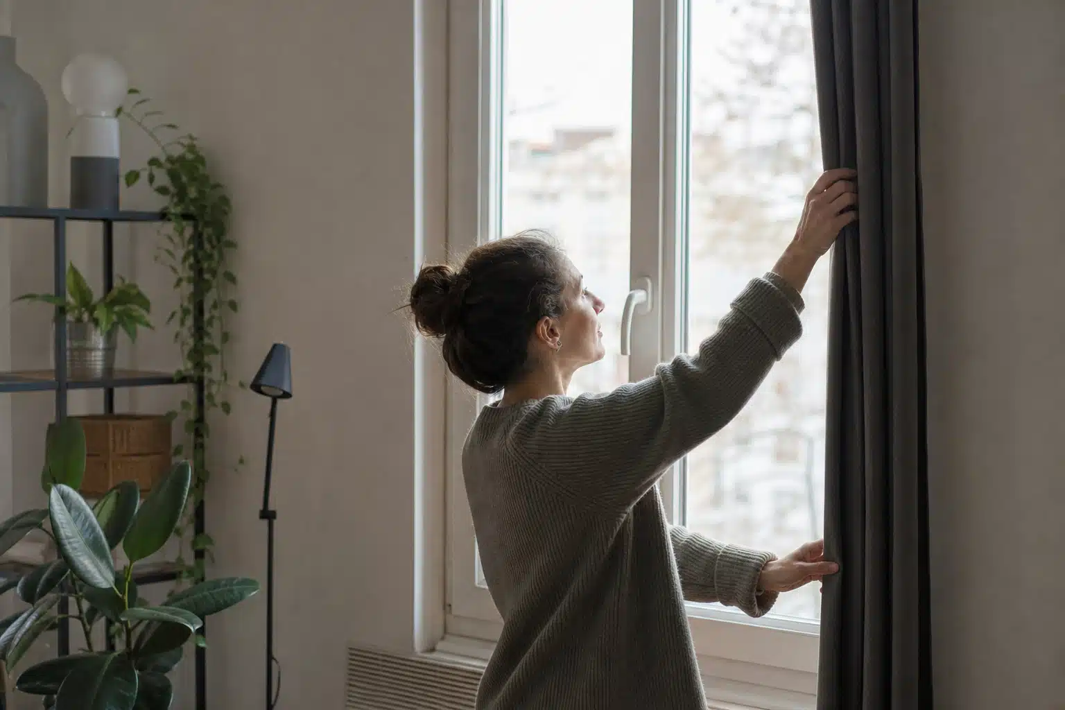 Femme ajustant les stores devant la fenêtre